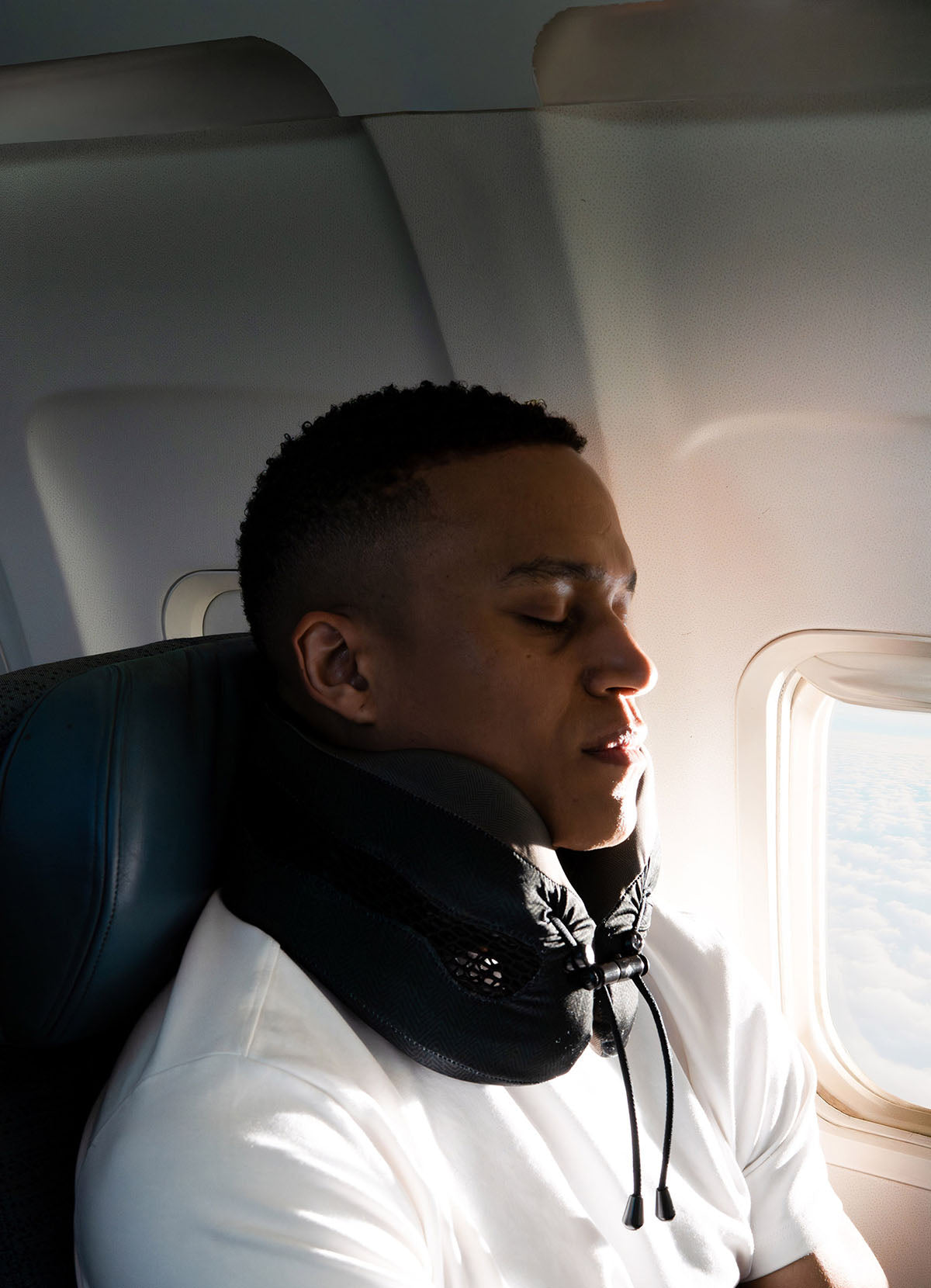 Man on an airplane with a neck pillow, looking out the window.